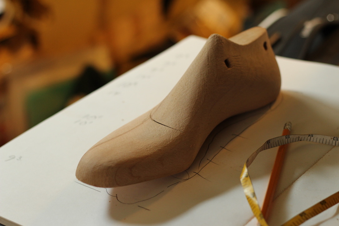 A wooden bespoke shoe last with pattern paper, pencil and measuring tape